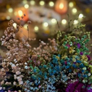 Bunte Trockenblumen mit Kerzen und unscharfen Lichtern im Hintergrund.