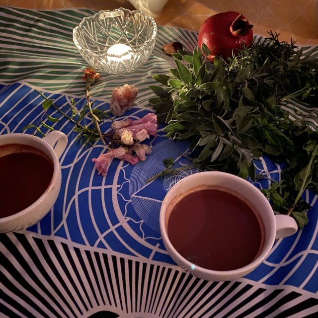 Zwei Tassen Tee auf einem bunten Tisch mit Früchten und frischen Kräutern.