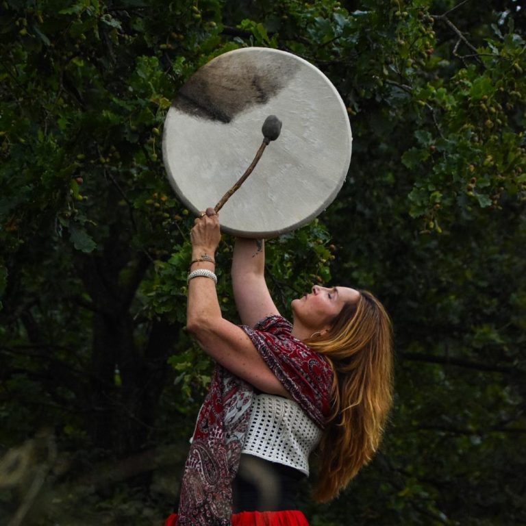 Ein sitzender Musiker mit Trommel und Schale, umgeben von Rauch und mystischer Atmosphäre.
